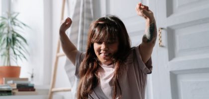 A relaxed Asian woman wakes up and stretches in a sunlit bedroom, enjoying the morning light.